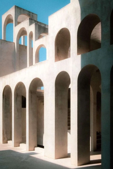 Architectural arches create geometric patterns in a sunlit courtyard, featuring modern design and a minimalist aesthetic on a clear day.