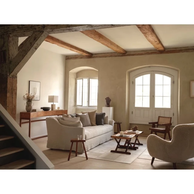 Interior of living room showcasing a sofa, wooden furniture, beige walls, and natural light from windows. Home decor and design.