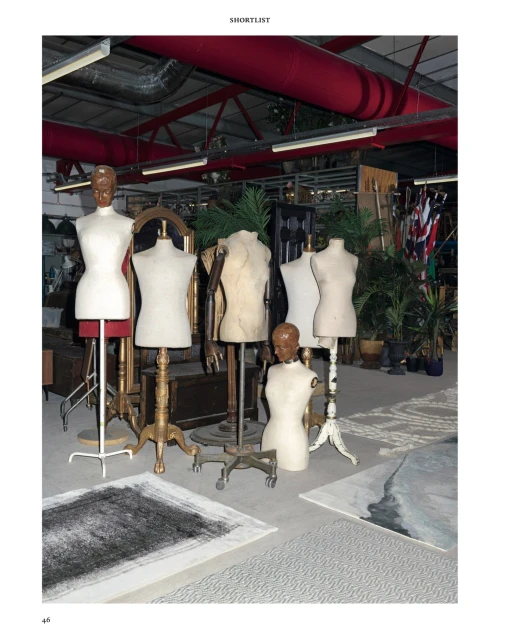 Group of dress form mannequins in an indoor location, possibly a warehouse or studio space, along with rugs and other miscellaneous items.