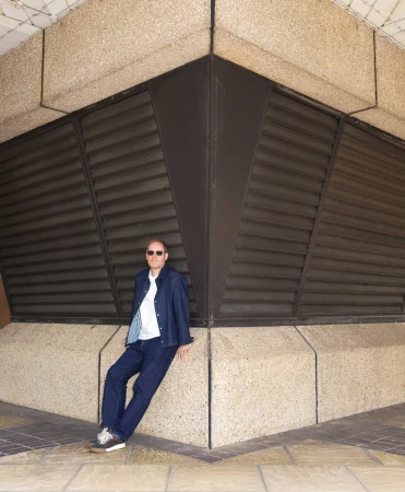 Man wearing a blue denim jacket leaning against a concrete column with dark louvers by photographer Frederike Helwig in London