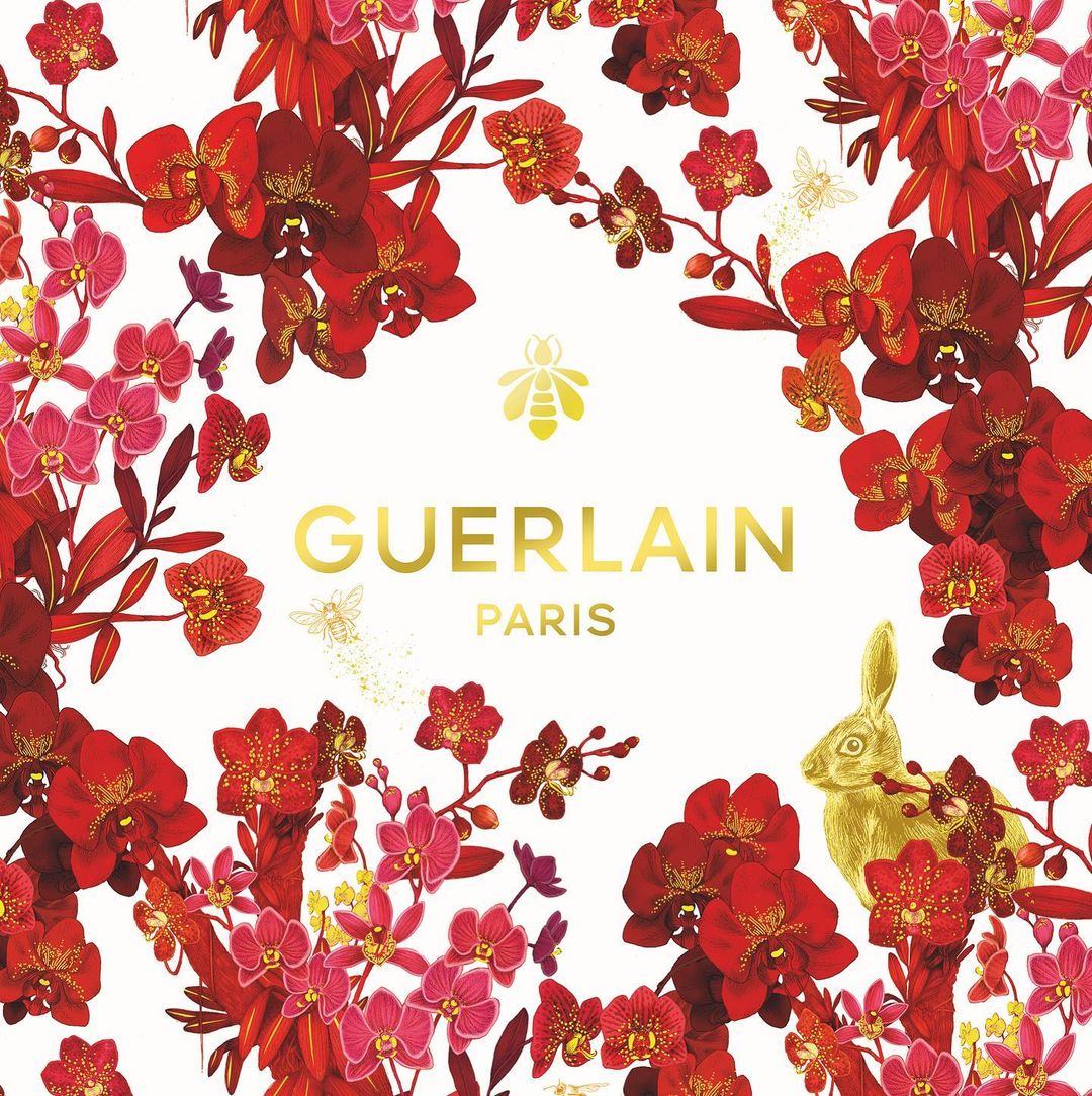 Guerlain logo and Paris text on a white background surrounded by a frame of red and pink orchids and leaves, with a golden rabbit.