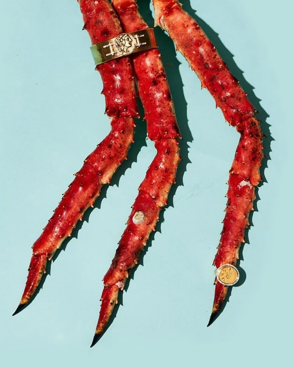 Close-up of three crab legs on a light blue background, adorned with gold jewelry, creating a striking and unexpected visual composition.