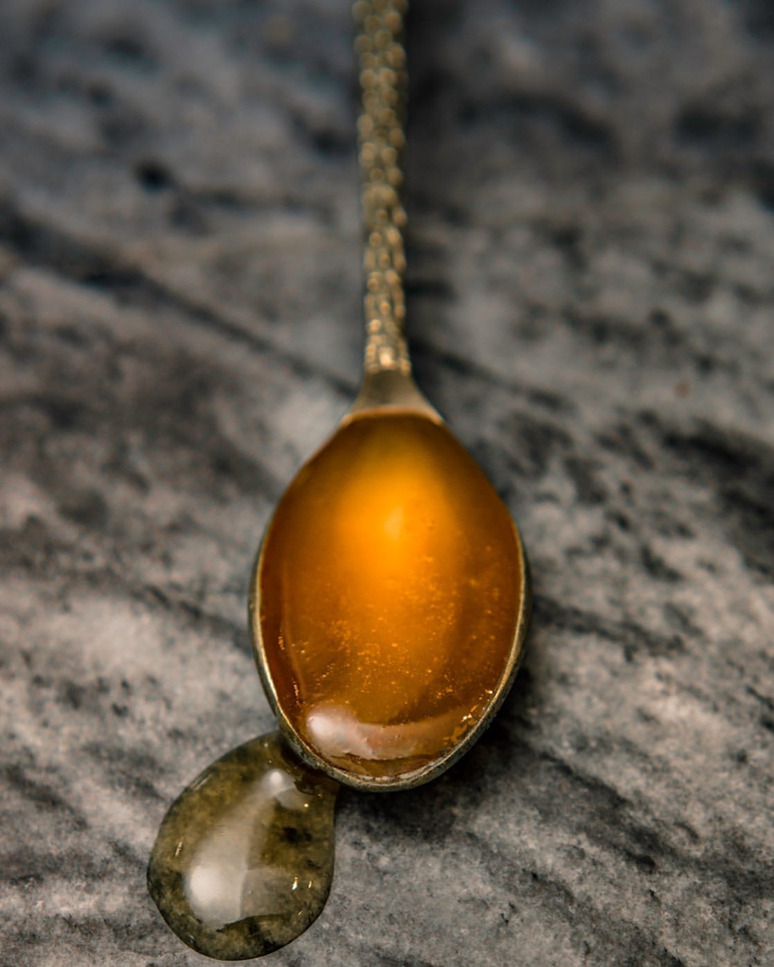 Close-up of honey on a vintage silver spoon with a drop falling onto a marble surface, creating a luxurious and appetizing scene.
