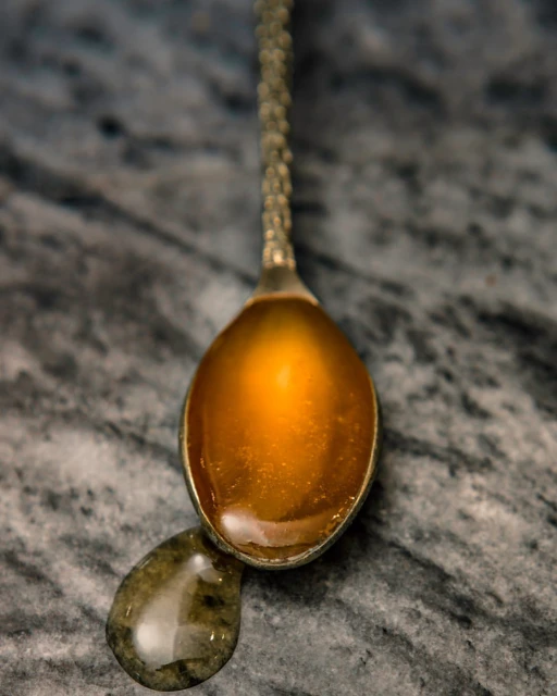 Close-up of honey on a vintage silver spoon with a drop falling onto a marble surface, creating a luxurious and appetizing scene.