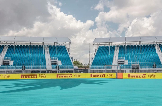 Outdoor shot of empty turquoise stadium seating under a cloudy sky. Pirelli banners line the front of the bleachers in yellow and red.