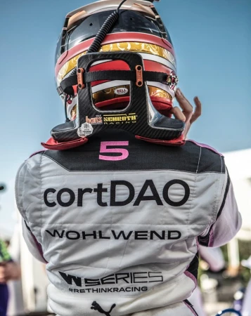 Close-up shot from behind of a racer wearing a helmet and racing suit with sponsors and text on the back, racing environment.