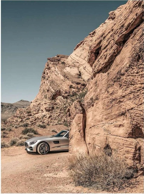 Silver convertible car parked near sandstone rock formations and arid desert vegetation, under a clear sky, creating a scenic automotive shot.