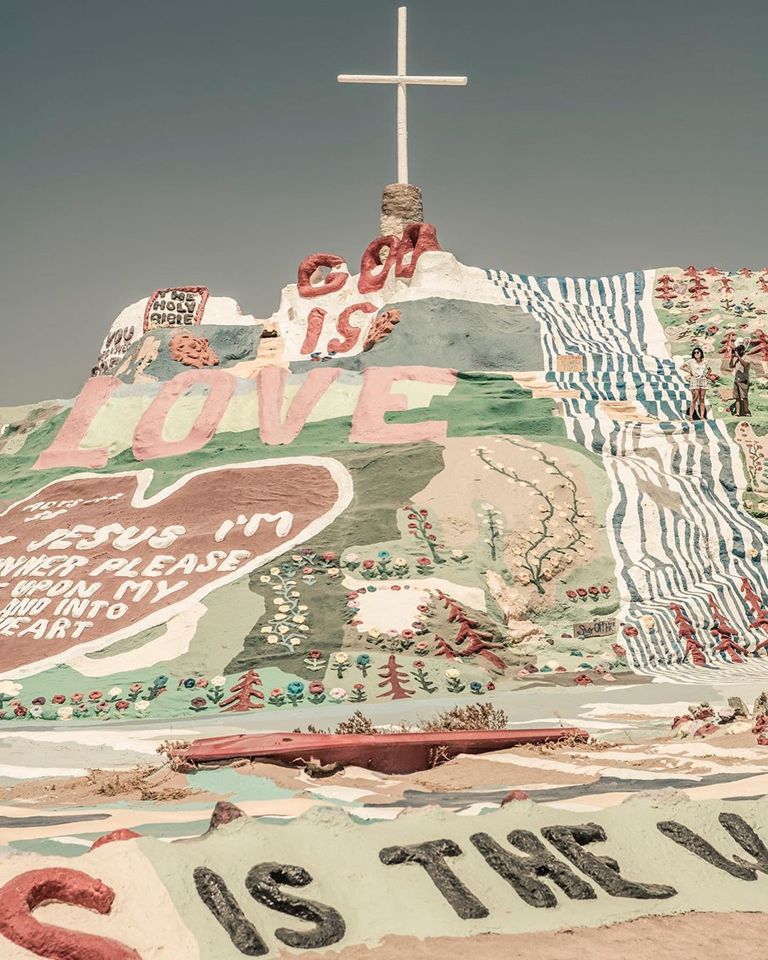 Salvation Mountain landscape featuring colorful paint, religious messages, and a white cross against a clear blue sky in Southern California.