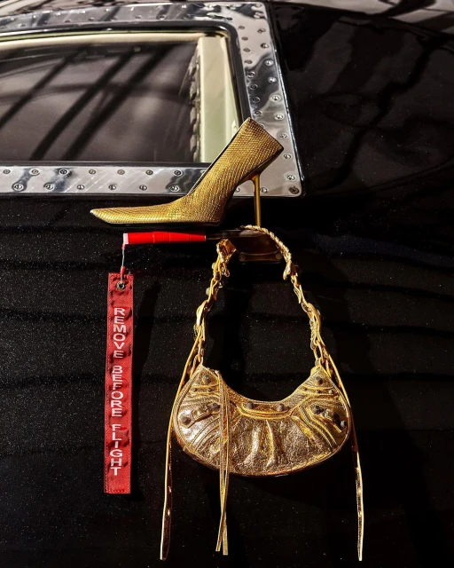 Gold high heel shoe and gold purse are suspended in an airplane cabin with a red 'remove before flight' tag visible.