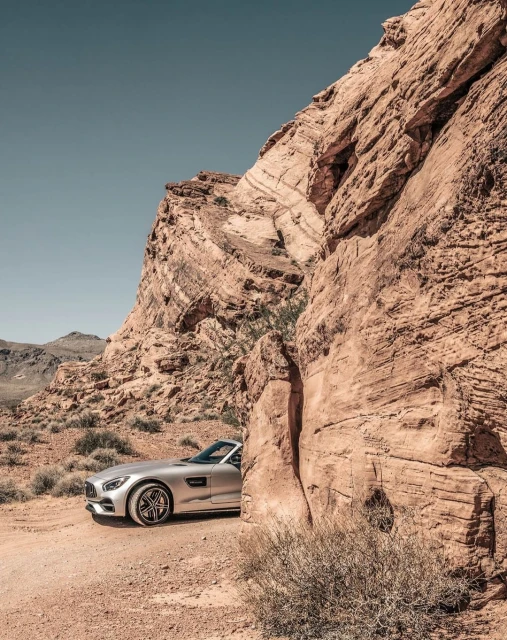 Silver sports car parked near towering red rock formations on a clear day, creating a striking contrast between machine and nature.