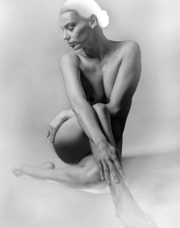Monochrome studio portrait of a seated woman posing with softly lit chiaroscuro lighting against a neutral background.