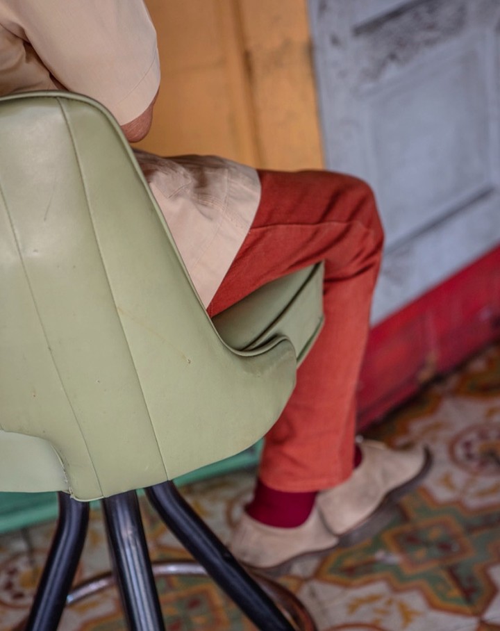Person seated in a green mid-century modern chair indoors with orange pants and tan shoes, offering a glimpse of casual style.