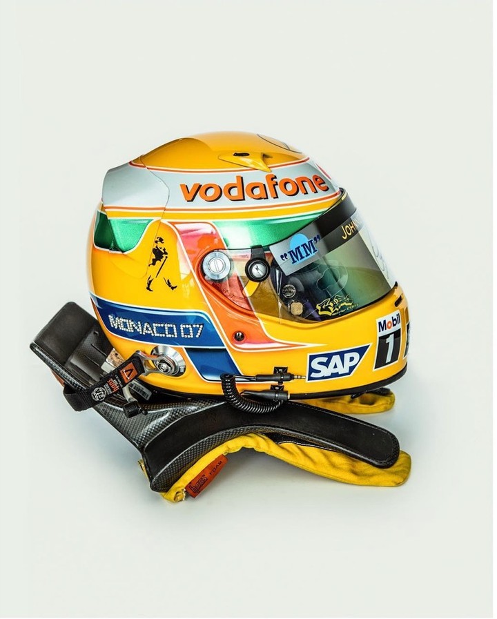 Racing helmet and gloves on a white background. The helmet is yellow with logos; the gloves are carbon fiber. Sport equipment.