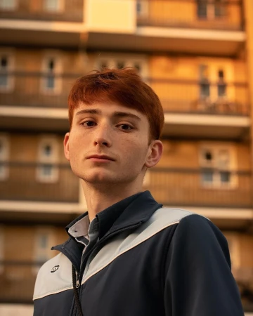 Young man with red hair wearing a blue and light grey zip-up jacket in London, photographed by Freya Najade.