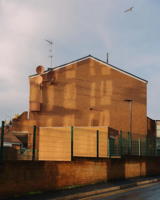 Urban landscape featuring a brick building with satellite dishes, street, and a bird in the sky, captured in warm light.