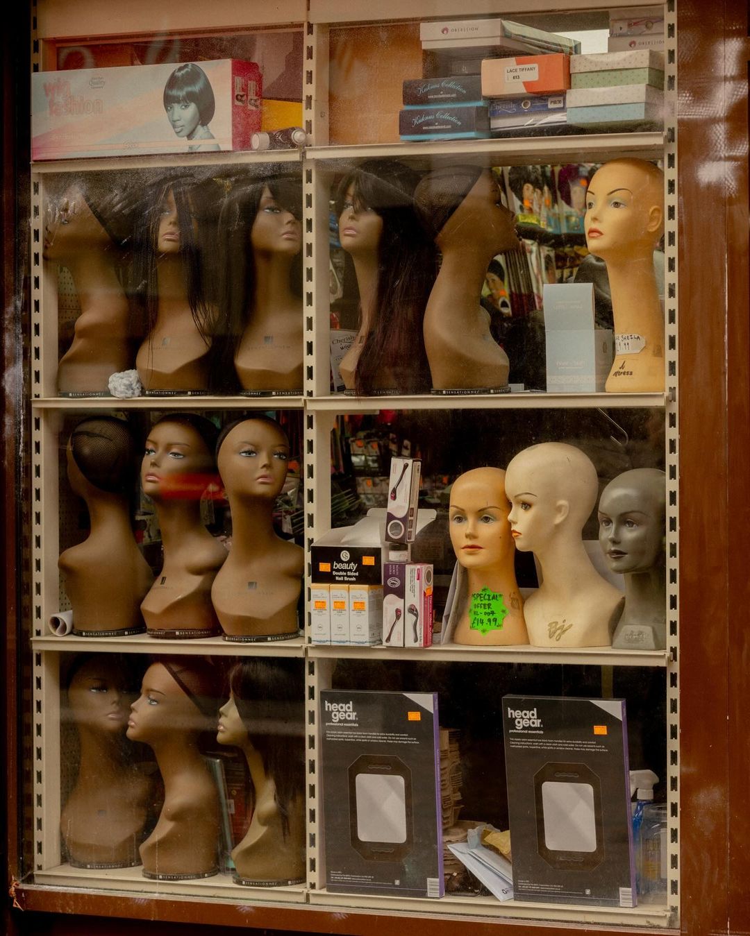Wig shop display featuring diverse mannequin heads with varying hairstyles, textures, and colors showcased in a storefront window.