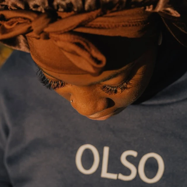 Eye-level portrait of a Black woman wearing a bonnet and a shirt with text; dramatic lighting creates contrast and shadow.