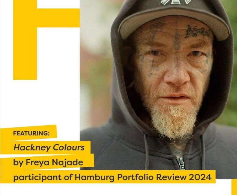 Portrait of a man with tattoos on his face and wearing a hooded sweatshirt, shot outdoors. He also wears a baseball cap.