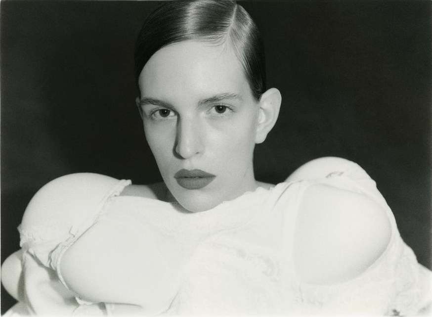 Striking black and white portrait of a woman with sleek hair and a fashion-forward bra top against a dark, moody background.