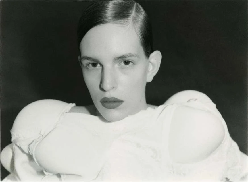 Striking black and white portrait of a woman with sleek hair and a fashion-forward bra top against a dark, moody background.