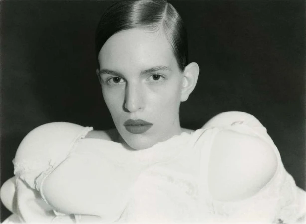 Striking black and white portrait of a woman with sleek hair and a fashion-forward bra top against a dark, moody background.