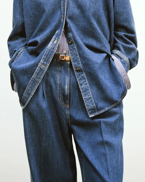 Denim fashion ensemble: a person wears a blue denim shirt, striped shirt, brown leather belt and denim pants against a white background.
