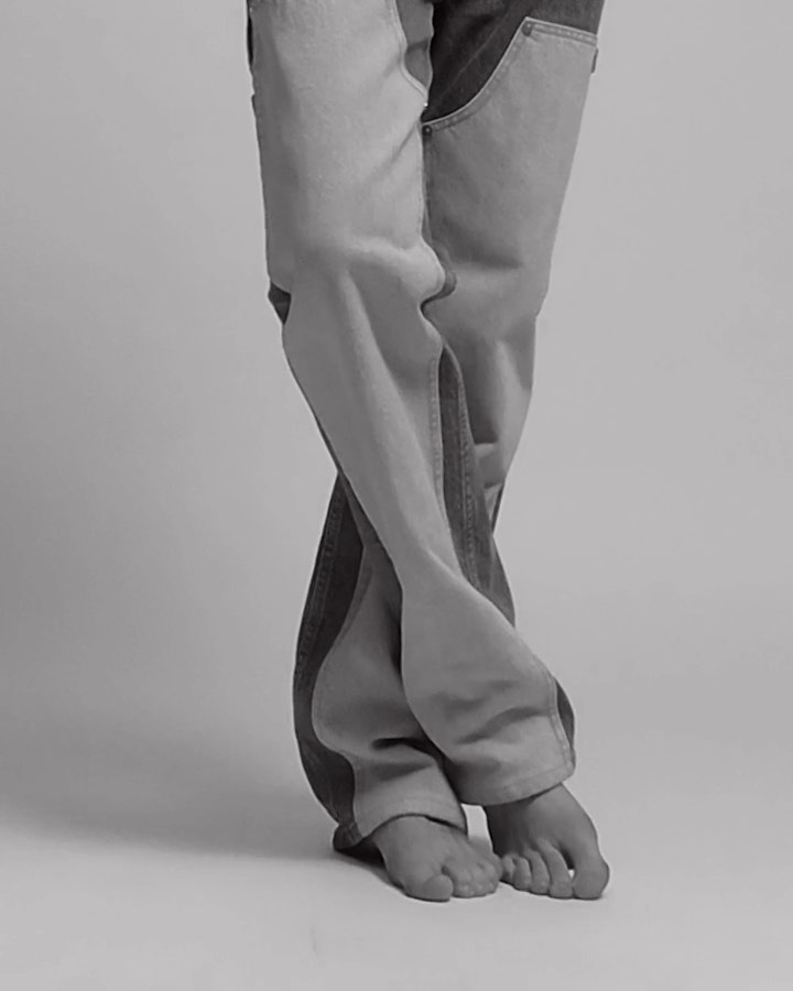 Fashion shot featuring person's legs wearing two-tone denim jeans in a studio with soft lighting and a neutral background, showcasing modern style.