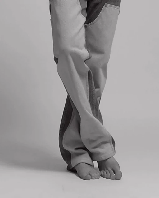 Fashion shot featuring person's legs wearing two-tone denim jeans in a studio with soft lighting and a neutral background, showcasing modern style.