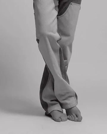 Fashion shot featuring person's legs wearing two-tone denim jeans in a studio with soft lighting and a neutral background, showcasing modern style.
