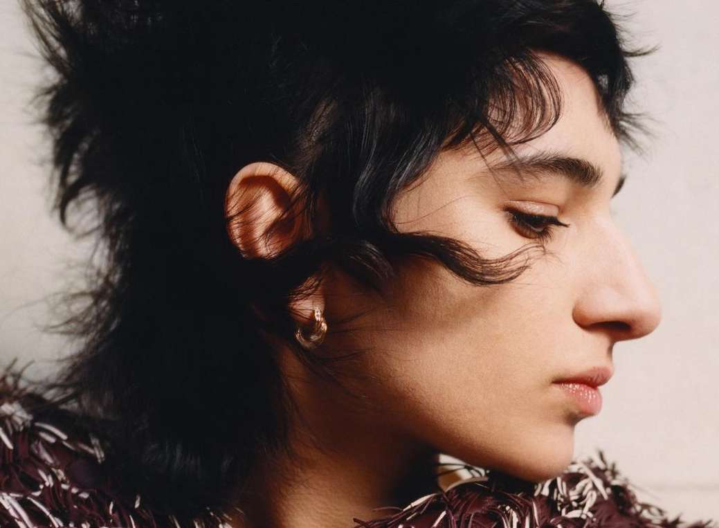 Close-up side profile of a young adult woman with dark hair, fair skin, and an earring. The shot highlights her face and jewelry.