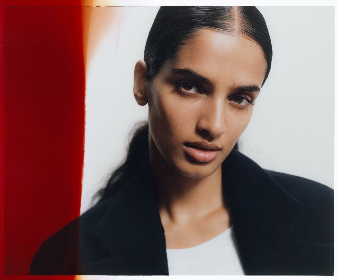 Close-up studio shot of a brunette woman wearing a black jacket, gazing directly at the camera against a bright white backdrop.