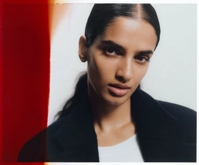 Close-up studio shot of a brunette woman wearing a black jacket, gazing directly at the camera against a bright white backdrop.