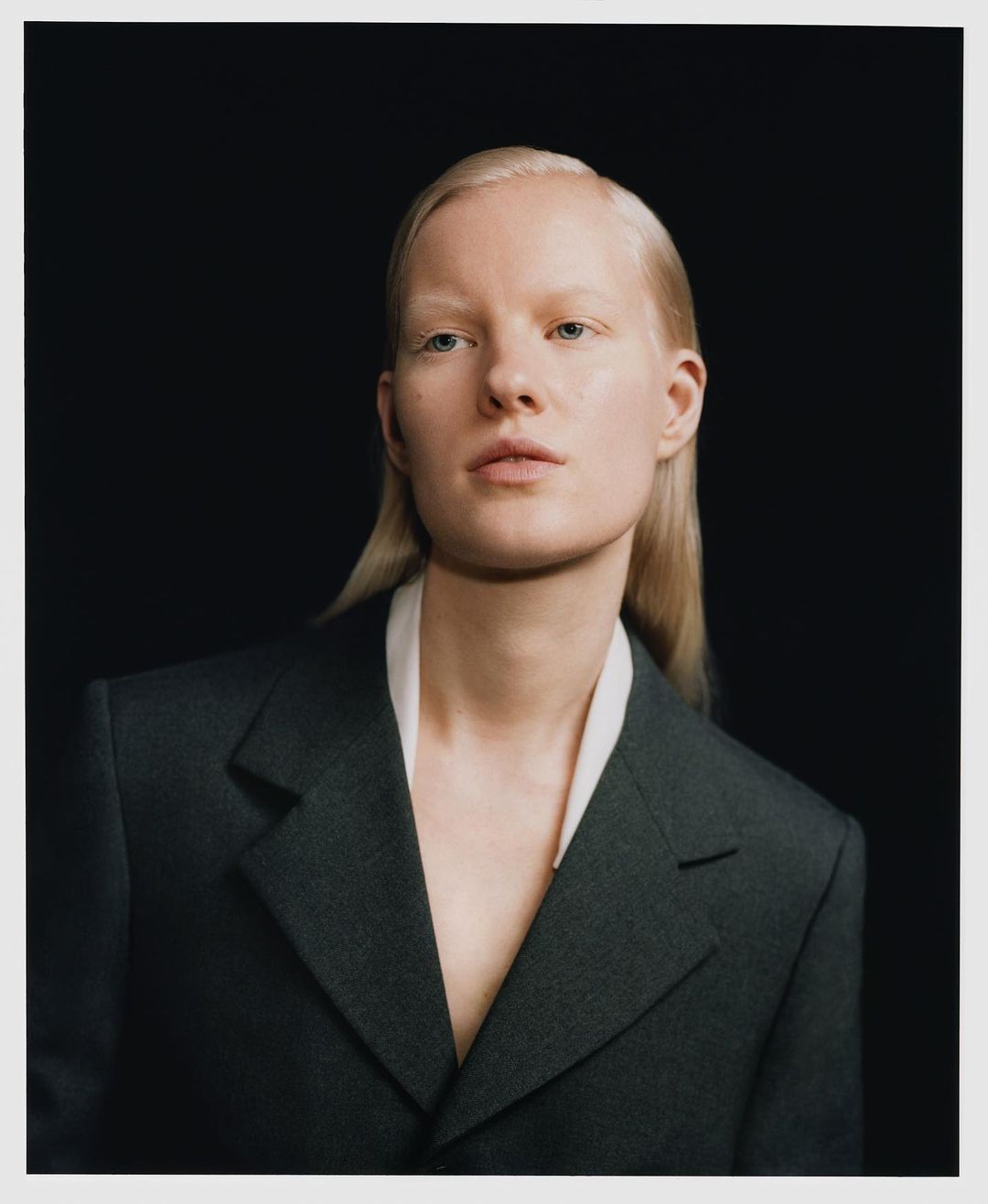 Portrait of an adult female with blonde hair, wearing a blazer, against a solid black background in a studio setting.