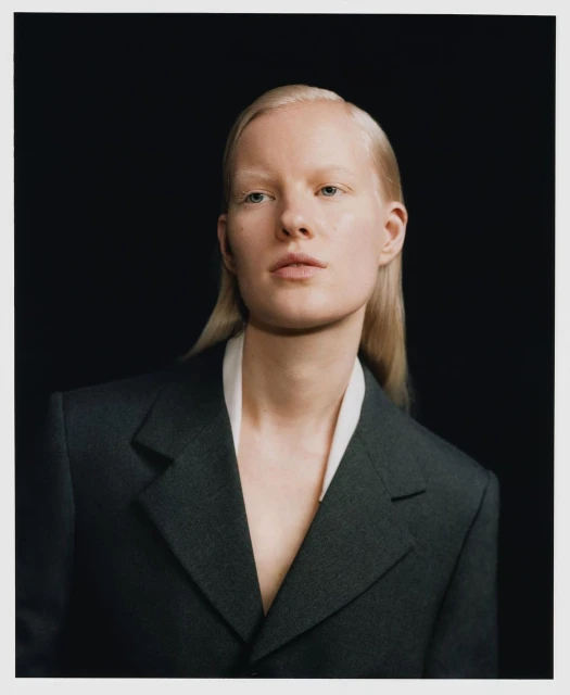 Portrait of an adult female with blonde hair, wearing a blazer, against a solid black background in a studio setting.