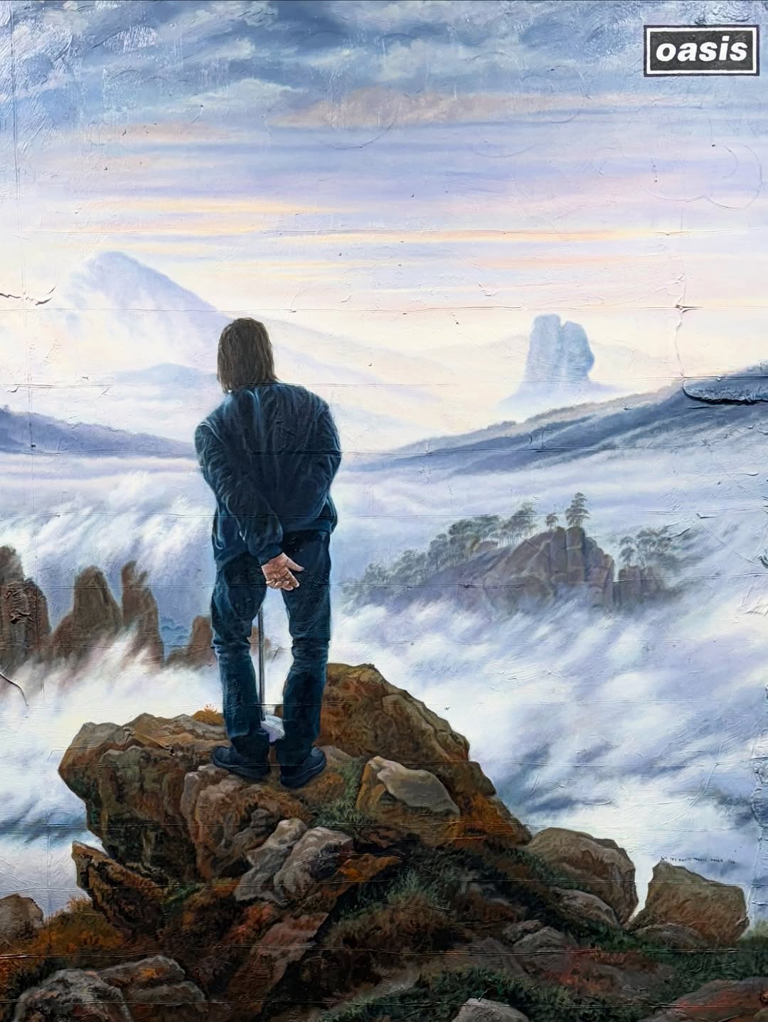 Painting of a man standing on a rocky outcrop overlooking a foggy mountain landscape. The artwork features cool blue and grey tones.