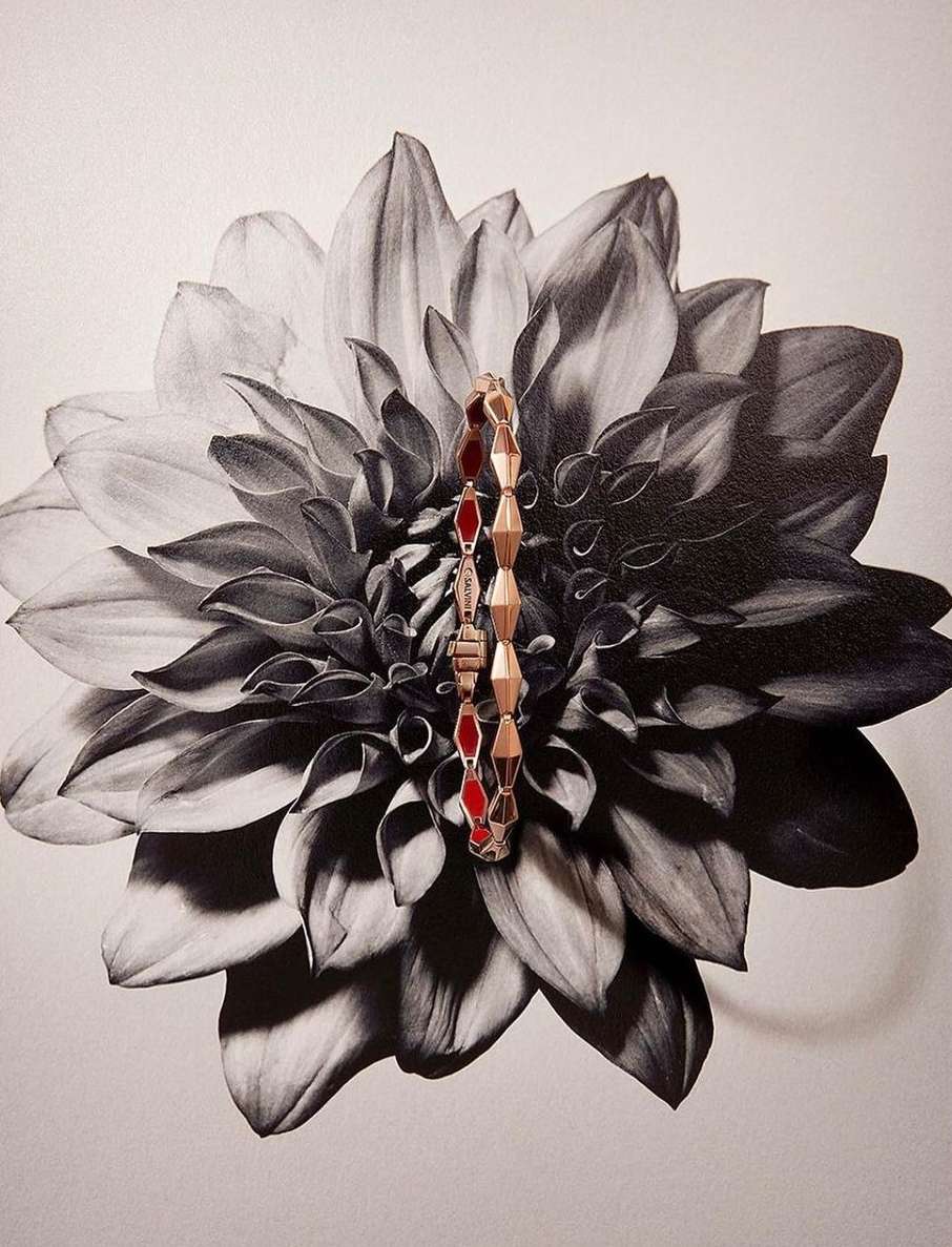 Close-up of a gold bracelet with red gems placed on a black and white flower, creating a striking contrast in color and texture.