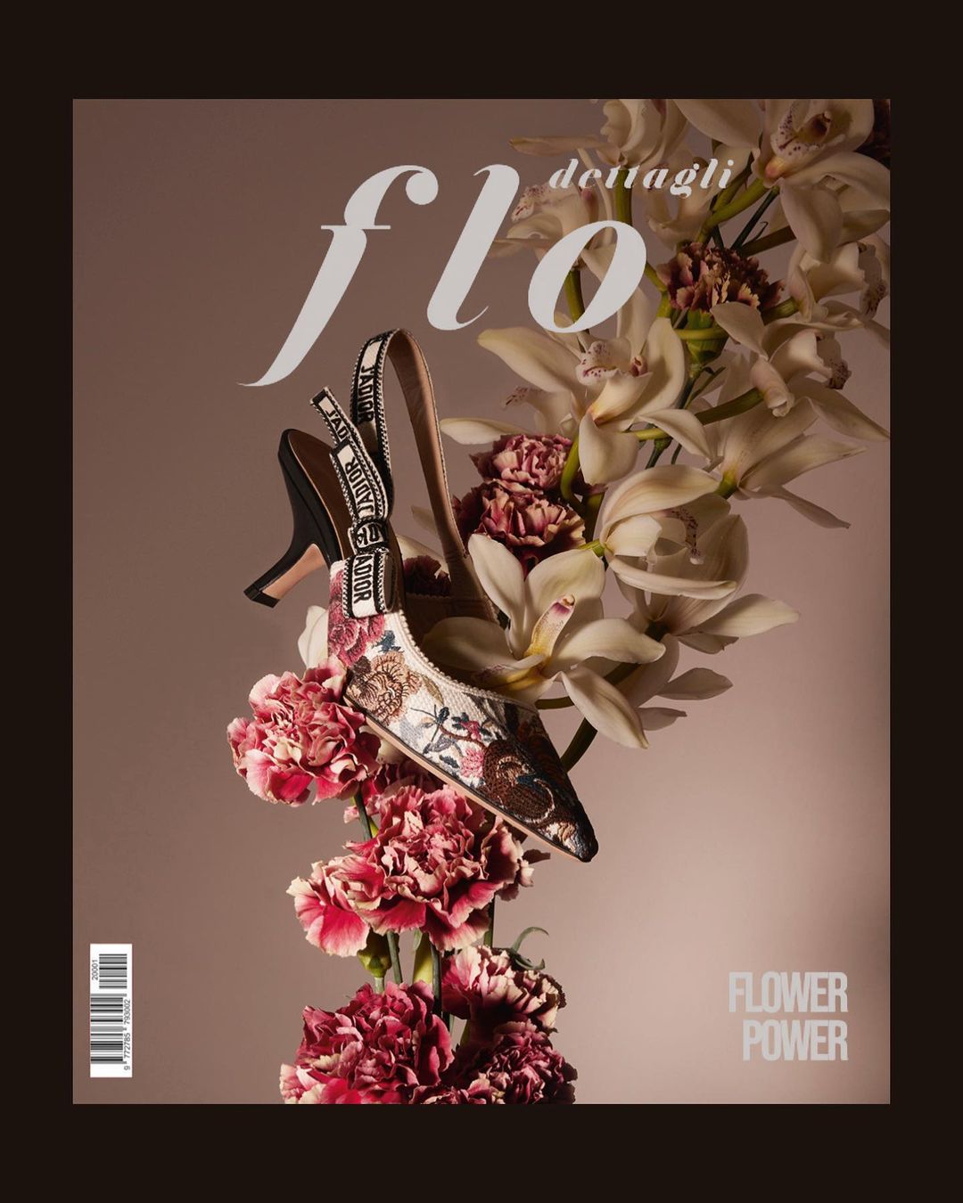 High-heeled slingback shoe with floral embroidery nestled among white orchids and dark pink carnations against a muted grey background