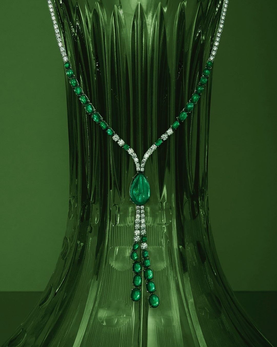 Elegant emerald and diamond necklace draped against a textured green backdrop, highlighting jewelry's sparkle and gem details.