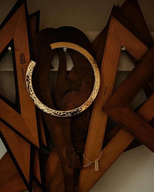 A golden collar necklace hangs in front of a wooden display comprised of wooden frames and shapes in a brightly lit setting.