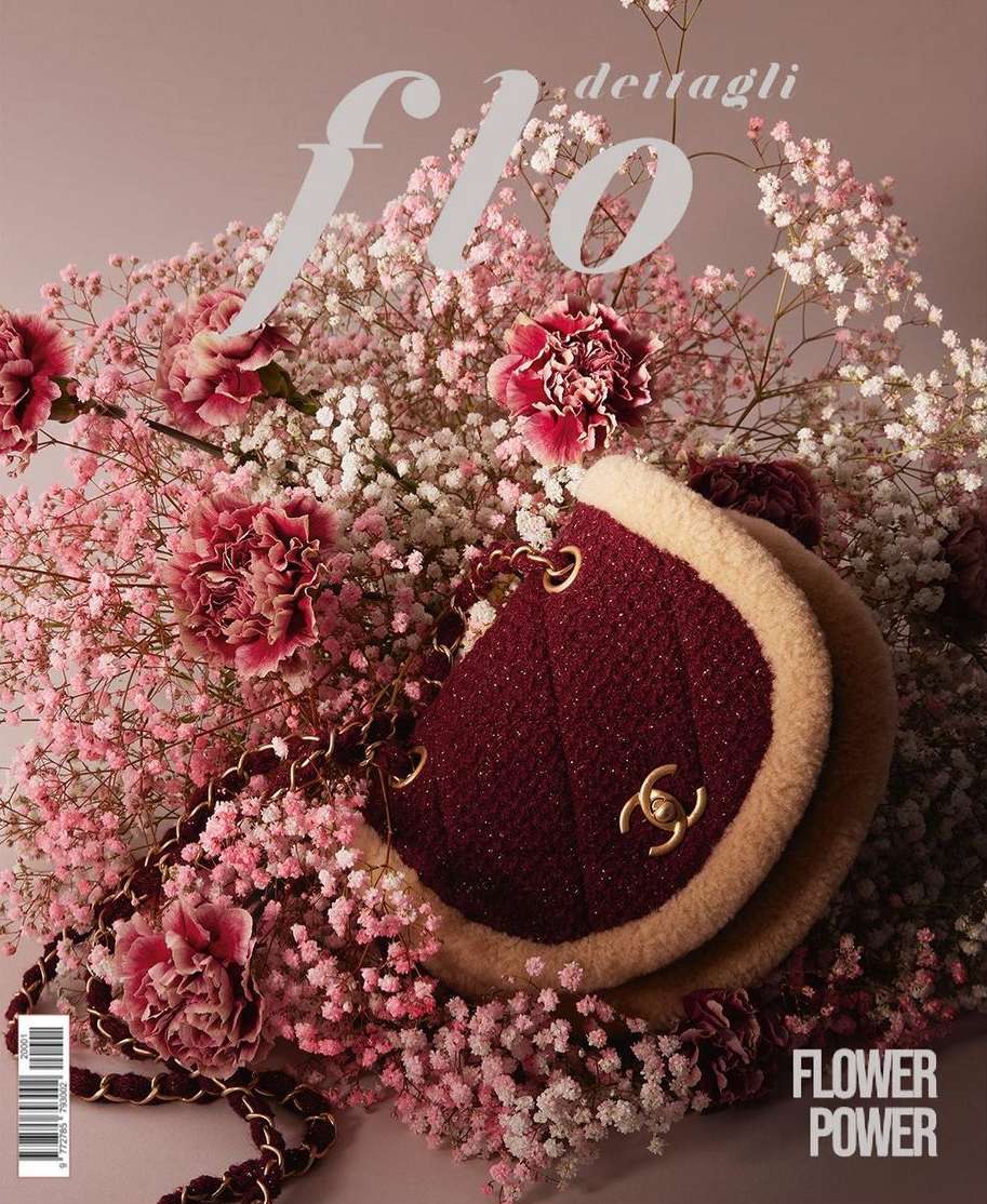 Burgundy Chanel handbag surrounded by white and pink baby's breath flowers and carnations, with a light purple background.