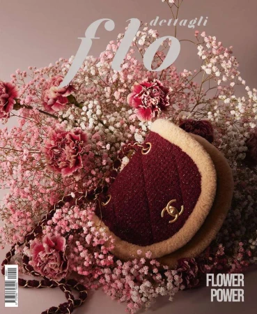 Burgundy Chanel handbag surrounded by white and pink baby's breath flowers and carnations, with a light purple background.