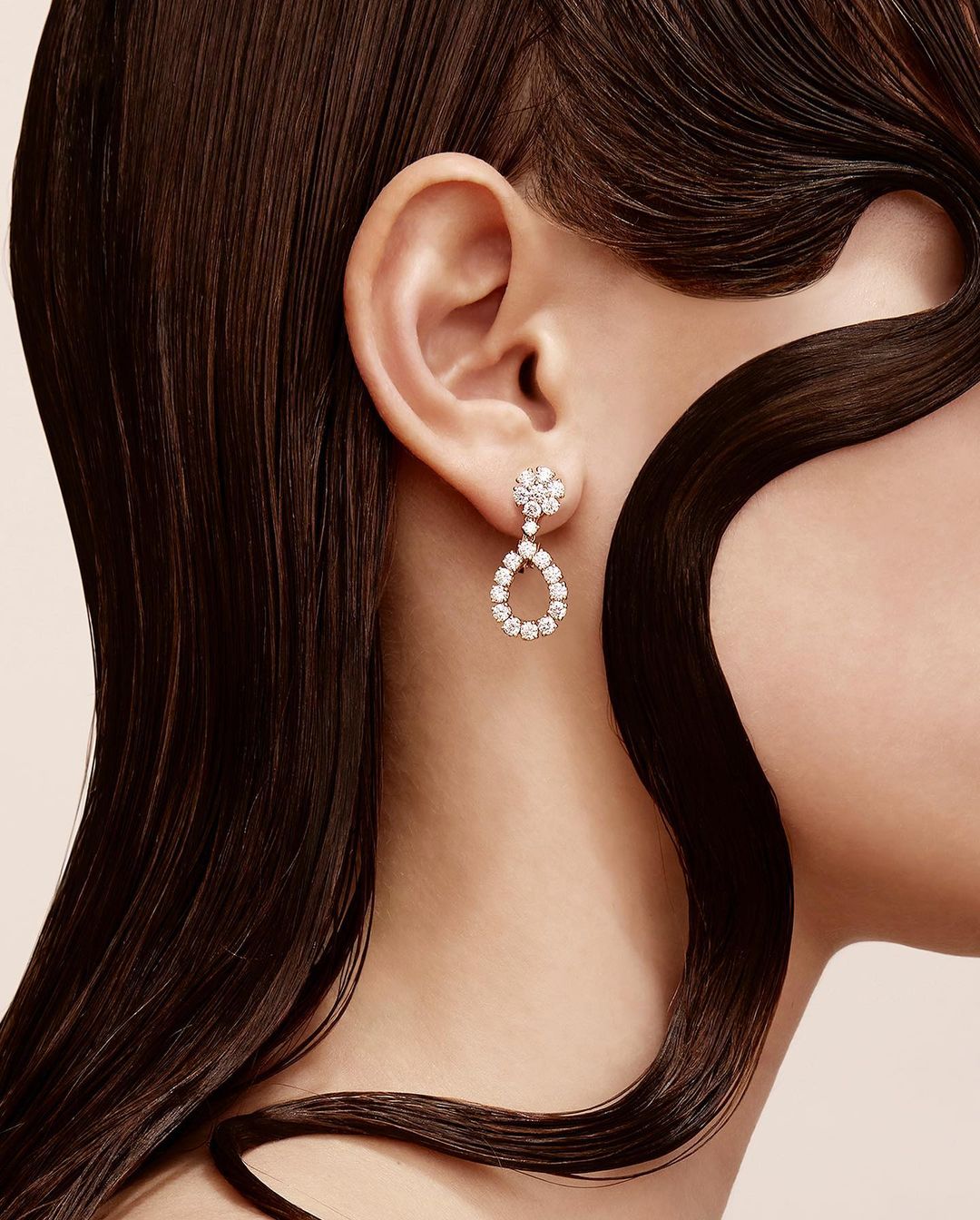 Close-up of a fair-skinned adult female wearing teardrop diamond earrings, with dark brown hair accentuating the jewelry and her ear.