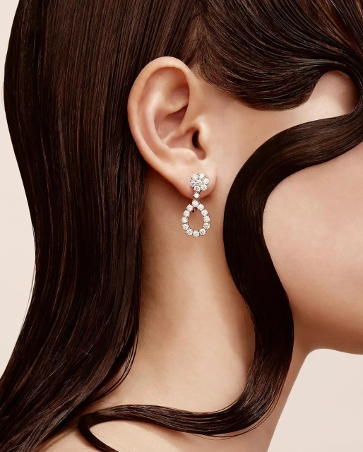 Close-up of a fair-skinned adult female wearing teardrop diamond earrings, with dark brown hair accentuating the jewelry and her ear.