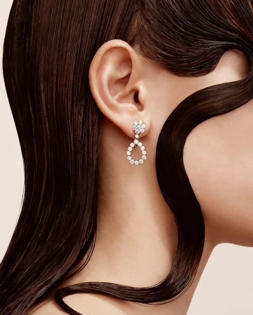Close-up of a fair-skinned adult female wearing teardrop diamond earrings, with dark brown hair accentuating the jewelry and her ear.