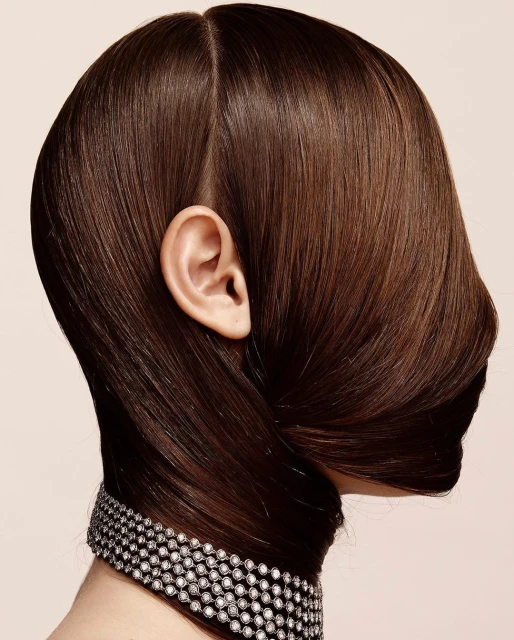 Close-up studio shot of a brunette woman's head and face, hair styled up, diamond choker necklace, light skin tone, and neutral backdrop.