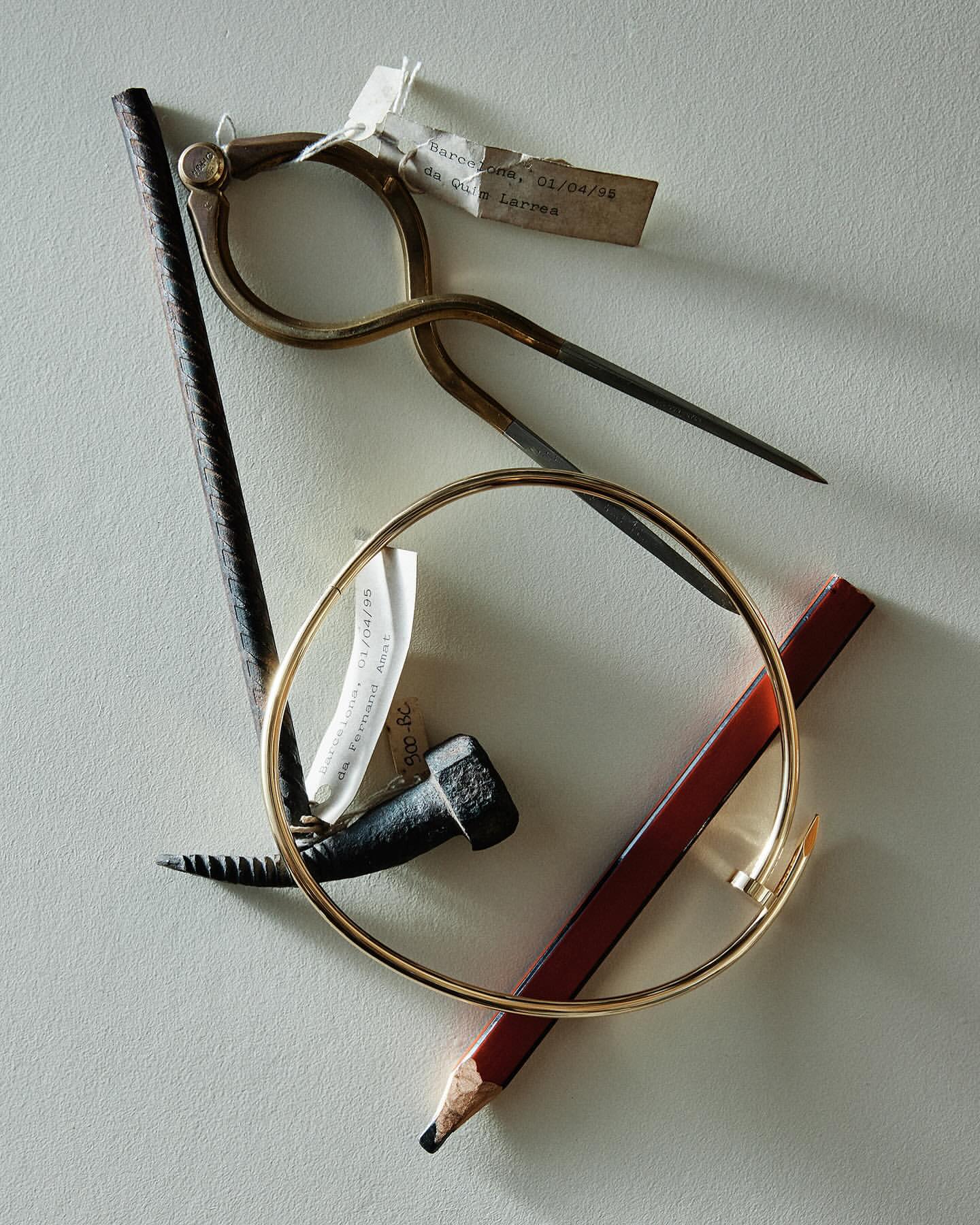 Still life of drafting compass, bracelet, nail, pencil and metal rod on neutral surface with label and geometric composition.