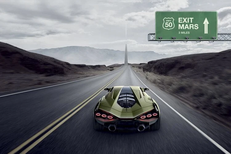Green sports car drives along a long desert road toward the horizon, a sign reads 'Exit Mars' on an overcast day.