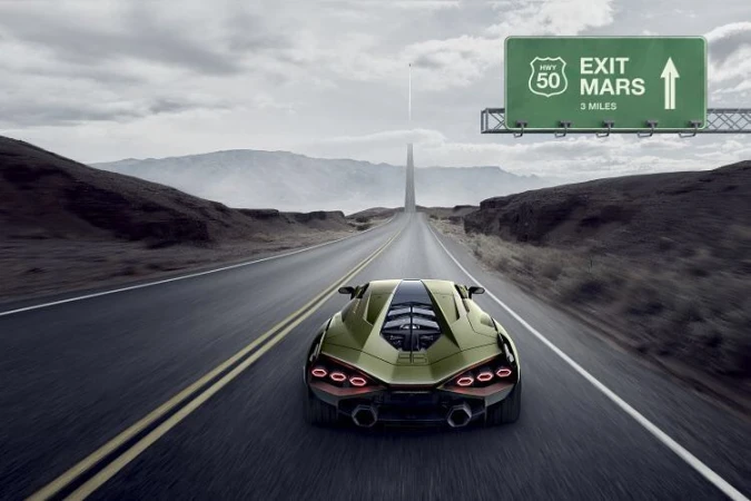 Green sports car drives along a long desert road toward the horizon, a sign reads 'Exit Mars' on an overcast day.