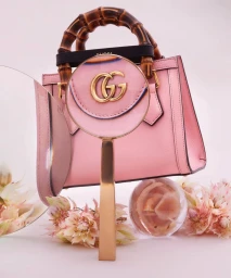 Pink leather handbag with bamboo handles behind a magnifying glass and delicate flowers by Fulvio Bonavia.