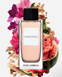 Dolce and Gabbana perfume bottle surrounded by vibrant pink flowers, watermelon slices, and wood shavings on a white background